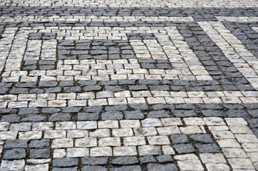 A geometrical pattern made from black and grey cobblestones, forming vertical and horizontal lines.