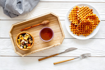 Fototapeta na wymiar Round belgian waffles for breakfast. Breakfast in bed. Waffles on plate. Honey and dried fruits in tray, knife and fork, tablecloth on white wooden background top view