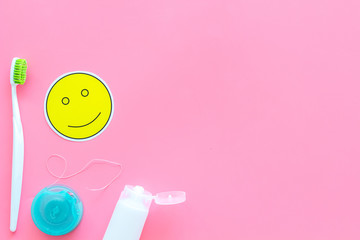 Set for daily teeth care. Toothbrush, tooth paste, dental floss near smile face emoji on pink background top view copy space