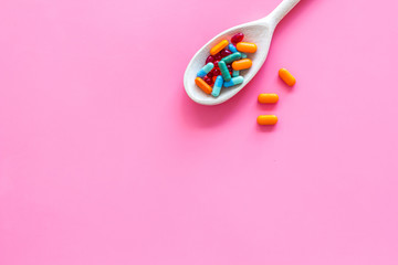 Reception of medicines concept. Pills in spoon on pink background top view space for text