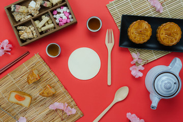 Fototapeta na wymiar Table top view aerial image of decorations Chinese Moon Festival or lunar new year background concept.Flat lay essential meal set for coffee break of sweet cake & tea with blossom on red paper.