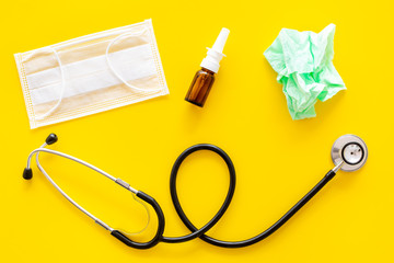 Flu drops. Running nose concept. Wrinkled napkin near stethoscope and face mask on yellow background top view