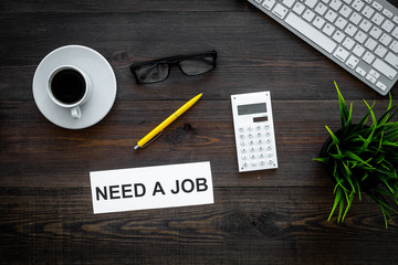 Need a job sign on office desk with computer keyboard on dark wooden background top view. Unemployment concept