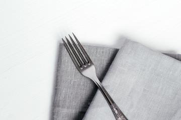 Steel fork and gray cloth napkins on a white wooden table - 219888758