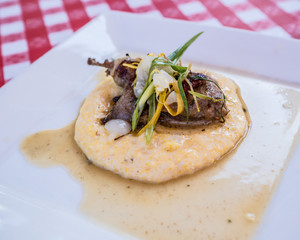 Gourmet cuisine of chicken or quail served on a white plate with a classic checkered table cloth.