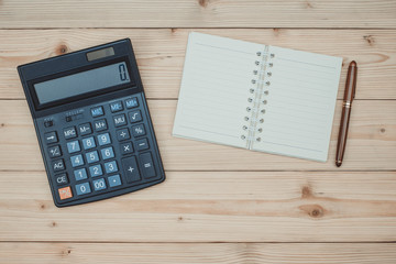 Office supplies or office work essential tools items on wooden desk in workplace, pen with notebook and calculator, top view