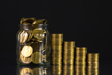 Coins stacks and gold coin money in the glass jar on dark background, for saving for the future banking finance concept.