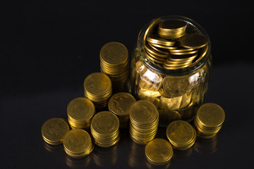 Coins stacks and gold coin money in the glass jar on dark background, for saving for the future banking finance concept.
