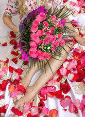 A girl sits on a bed with a pink bouquet of flowers. A gift for the holiday. Female feet.