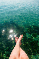 Two pale legs over bright blue clear water on a very sunny day