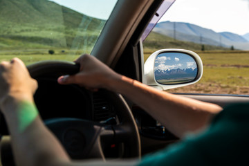 driving car on the mountain road. Guy inside the car driving on the country roadway between fields with brown grass and snowy mountains . Sun is shining. Shoot from the back.