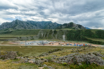 Panoramic view of large-scale construction of an industrial facility in the mountains with the help of cranes, trucks and other special equipment against the blue sky