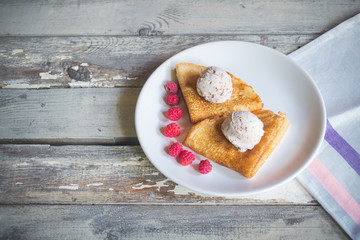 Crepes with ice cream with chocolate chips and fresh raspberries on aged wooden background.