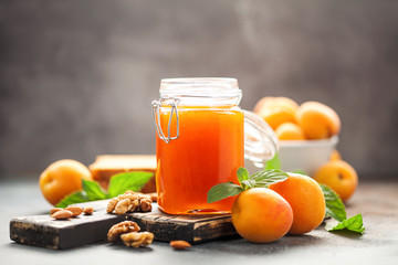 Apricot jam in a jar and fresh fruits with nuts on  wooden cutting board. Healthy breakfast