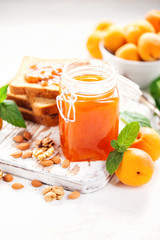 Apricot jam in a jar and fresh fruits with nuts on  wooden cutting board. Healthy breakfast