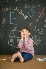 A small student on the background of a school board took his hands on his face posing a difficult task