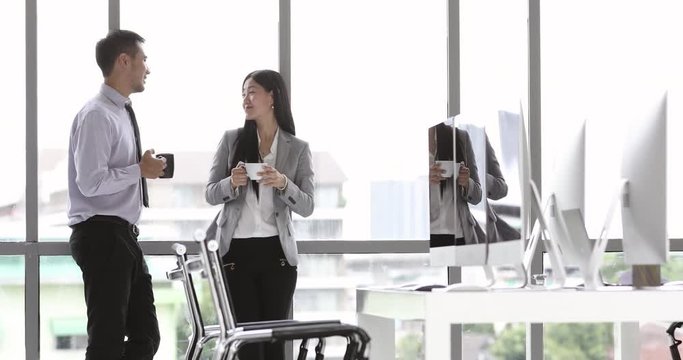 Businessman and businesswoman standing and drinking coffee while talking in modern office