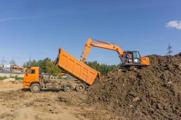 Orange excavator loads the land on a construction site..