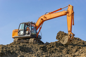 Orange excavator loads the land on a construction site.. © Makeev Petr