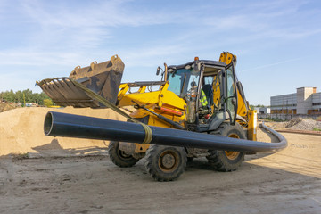 Tractor carries a long pipe for water supply at the construction site