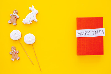Fairy tales book near gingerbread man and candies on yellow background top view space for text