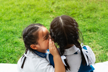 Two young girls whispering and sharing a secret during playground session on green glass background