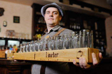 a man at the Oktoberfest festival in traditional Bavarian clothes and a hat holds a meter of beer and smiles