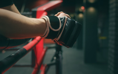 Boxing gloves on the fighter hands on the ropes of the boxing ring.