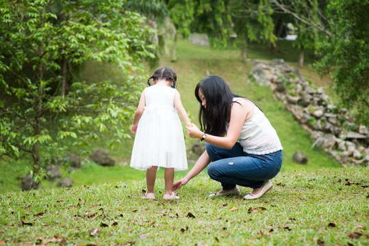Mother helps little girl wearing shoe at park