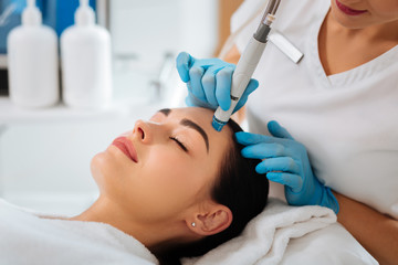 Professional cosmetology. Smart skilled cosmetologist using a modern device while doing hydrafacial...