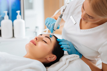 Obraz na płótnie Canvas Cosmetology clinic. Professional female cosmetologist doing hydrafacial procedure while being a work