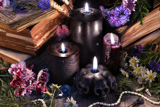 Still life with three black candles, old books, tarot cards and herbs with flowers. Mystic background with ritual esoteric objects, occult, fortune telling and halloween concept