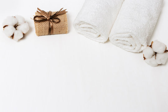White flower of cotton plant, two white cotton towels and soap on white concrete background with copy space.  Items for spa at home. Top view.