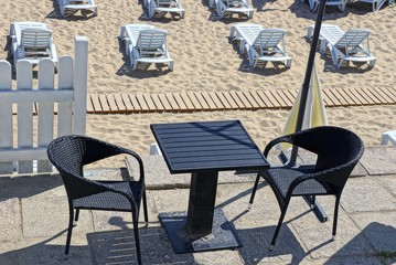 black table and chairs on the restaurant area and plastic white sunbeds in the sand on the beach