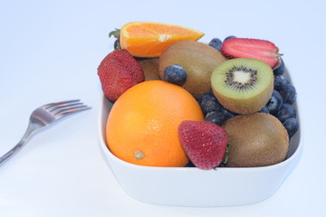 fresh fruits in white bowl on white background isolated with fork with copy space