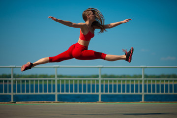 Young caucasian girl performs twine jumping on sky backround.