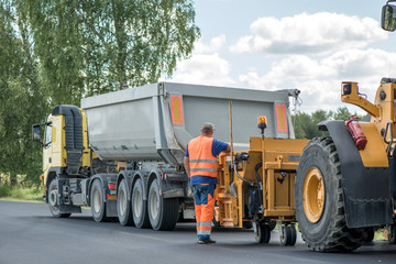 Road construction workers repairing highway road on sunny summer day. Loaders and trucks on newly made asphalt. Heavy machinery working on street. Road curbs being constructed with gravel