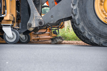 Spinning brush cleaning newly laid asphalt. Road construction workers repairing highway road on sunny summer day. Heavy machinery working on street. Road curbs being constructed with gravel