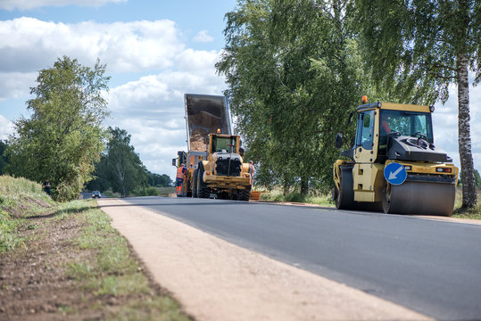 Road construction workers repairing highway road on sunny summer day. Loaders and trucks, heavy vibration roller compactor with arrow road sign on newly made asphalt. Work inspection with drone  
