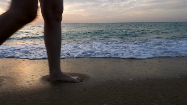 Woman feet walking in the water on the beach at the sunrise