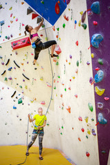 Photo of young woman exercising on wall for climbing and a trainer with a safety rope indoors