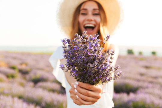 Cheerful young girl in straw hat holding lavender bouquet