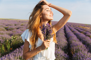 Photo of pretty european woman in dress holding bouquet with flowers, while walking outdoor through...