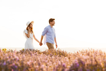 Cute loving couple walking in the lavender field outdoors holding hands of each other.