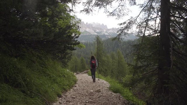 Mujer andando por un camino de piedras entre árboles con vistas a un valle en Dolomitas, Alpes Italianos