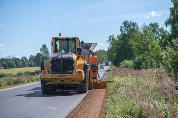 Road construction workers repairing highway road on sunny summer day. Loaders and trucks on newly made asphalt. Heavy machinery working on street. Road curbs being constructed with gravel