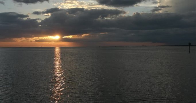 Tighter shot of the setting sun as it emerges from behind ominous storm clouds to cast its rays on central Florida's gulf coast. Frame right, a thunderstorm is raging over the gulf. 