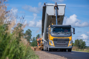 Road construction workers repairing highway road on sunny summer day. Loaders and trucks on newly made asphalt. Heavy machinery working on street. Road curbs being constructed with gravel