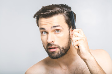 Portrait of handsome young man combing his hair in bathroom. Isolated over grey background.