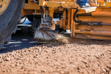Spinning brush cleaning newly laid asphalt. Road construction workers repairing highway road on...